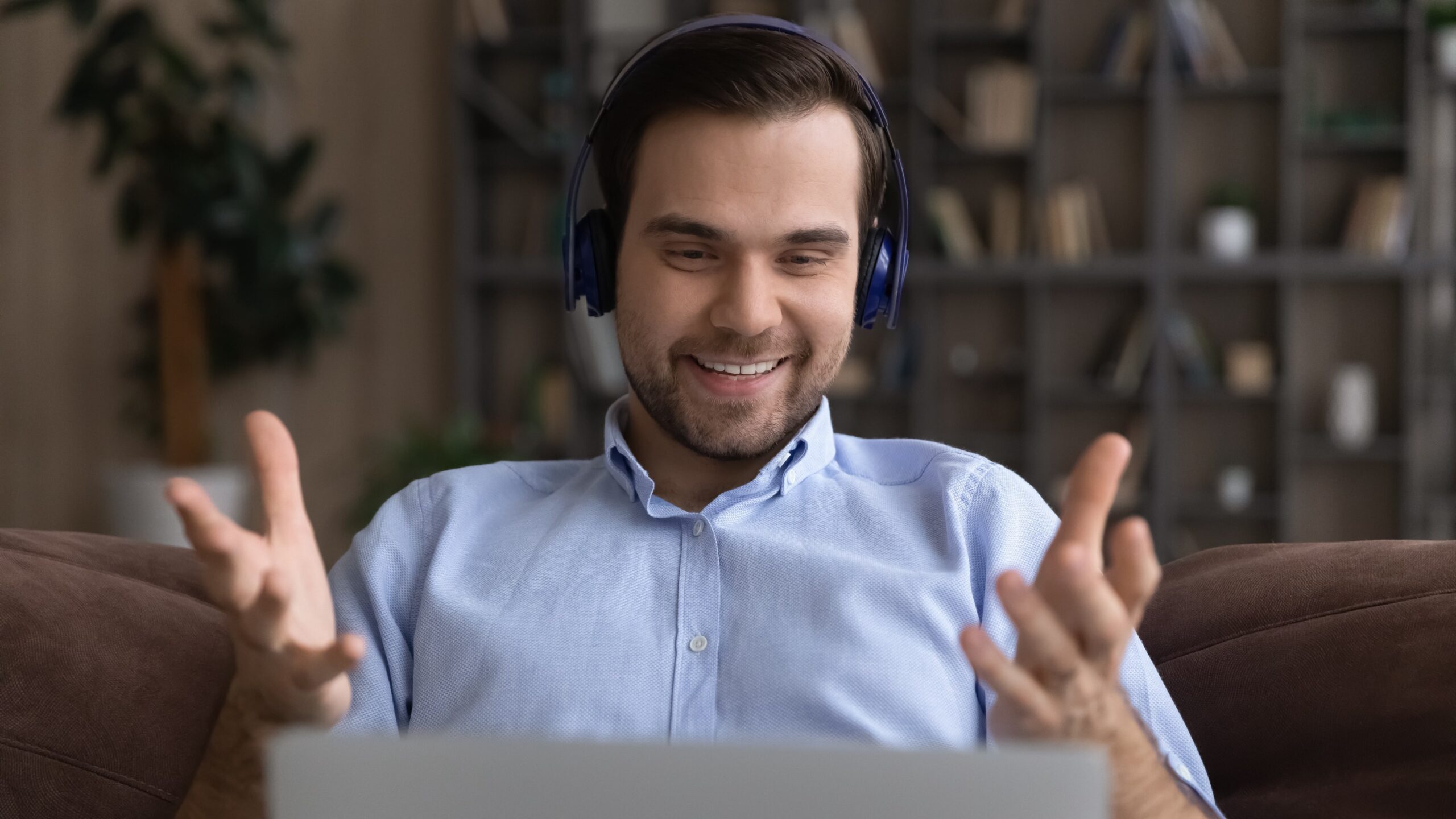 Man sitting behind laptop wearing headphones aand smiling at his screen.